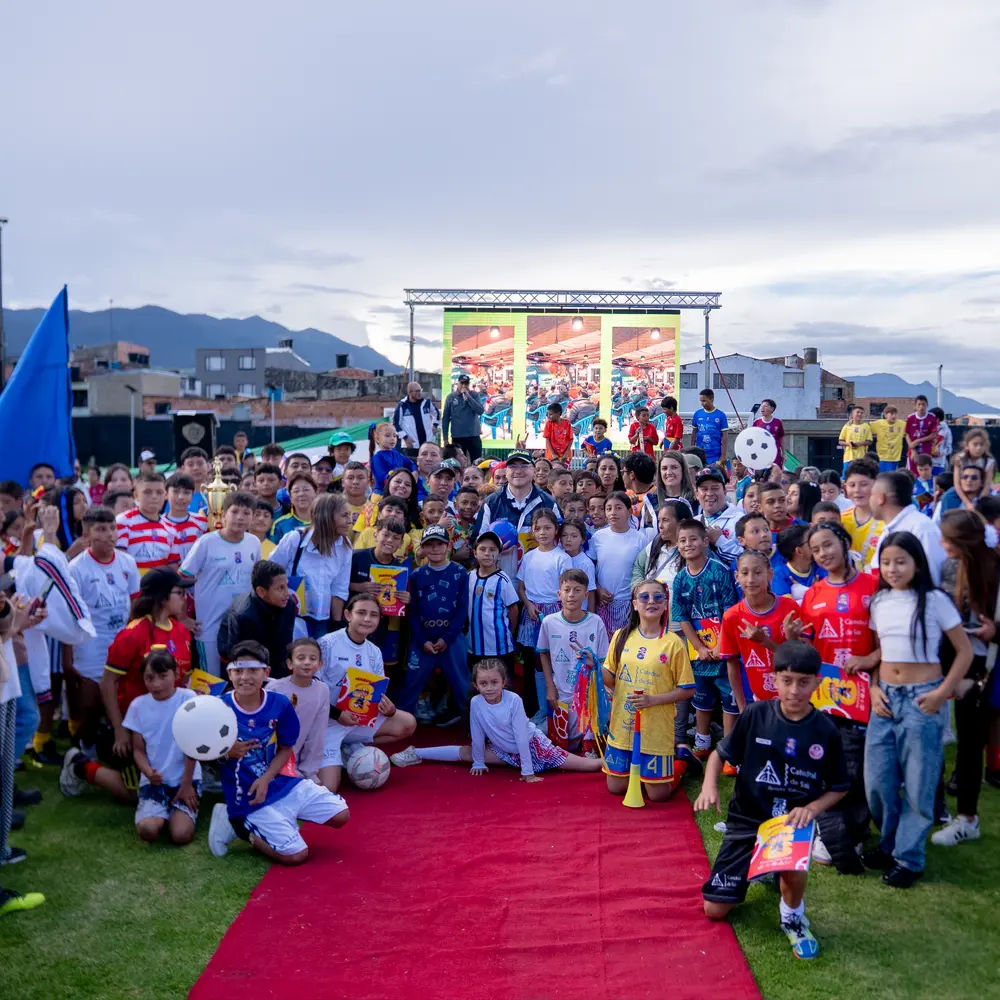 Gran grupo de niños participantes, familias y organizadores reunidos sobre una alfombra roja en la cancha durante la celebración del Mundialito 2026 patrocinado por la Catedral de Sal