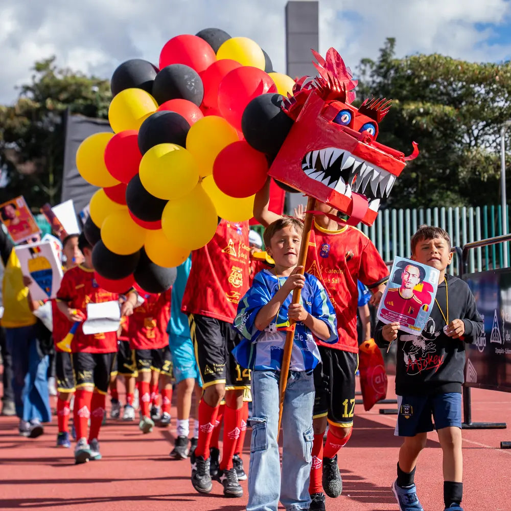 Niños de Zipaquirá marchan en el desfile del Mundialito 2026 portando una cabeza de dragón artesanal y globos con los colores de Bélgica.