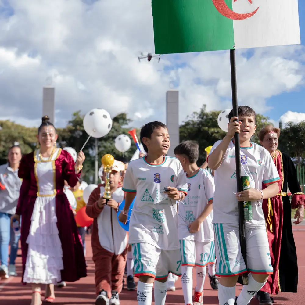 Un grupo de niños futbolistas lidera un desfile en la pista atlética portando la bandera de Argelia durante el torneo de la Catedral de Sal.