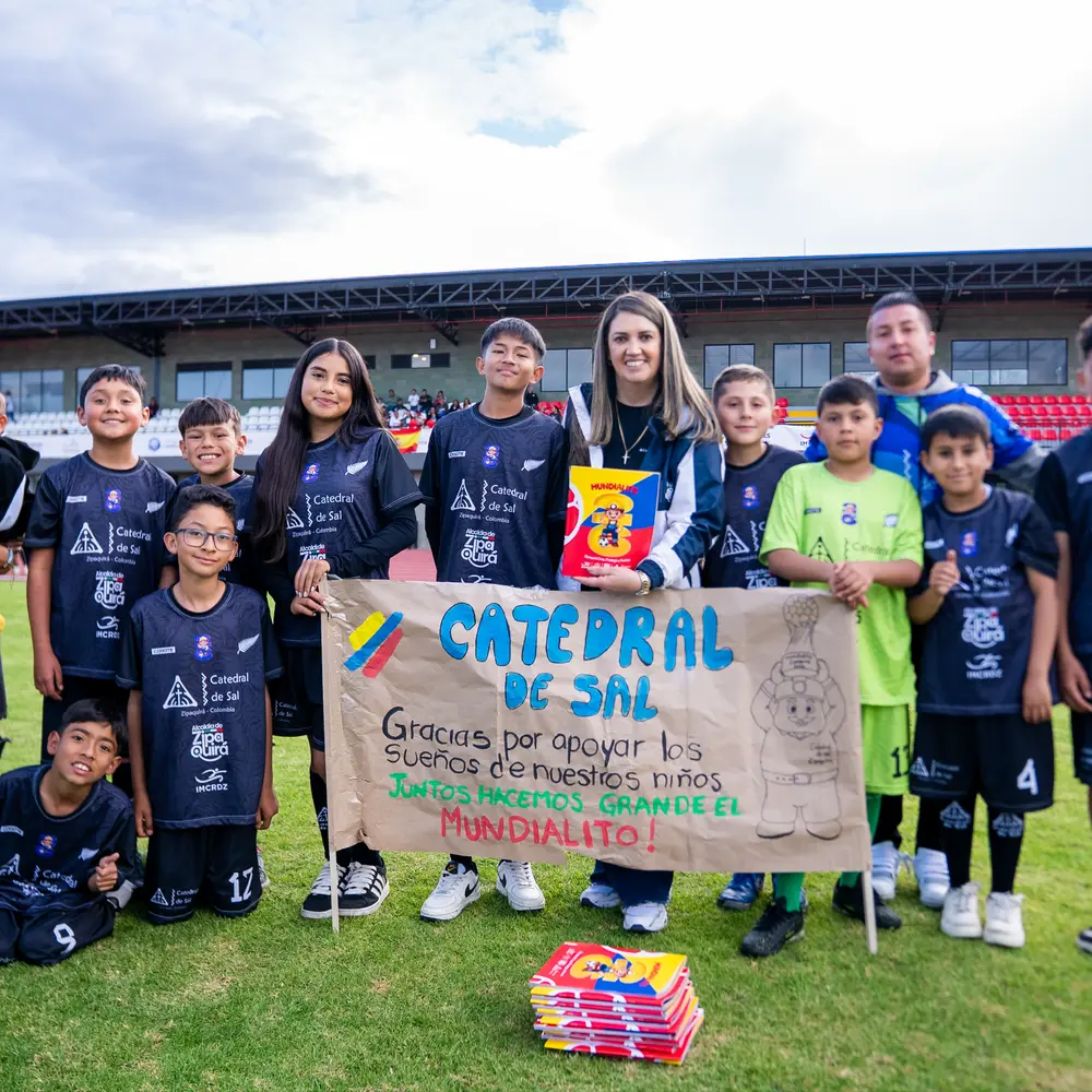 Un grupo de niños futbolistas posa junto a organizadores sosteniendo una pancarta de agradecimiento a la Catedral de Sal durante el torneo Mundialito 2026 en Zipaquirá.