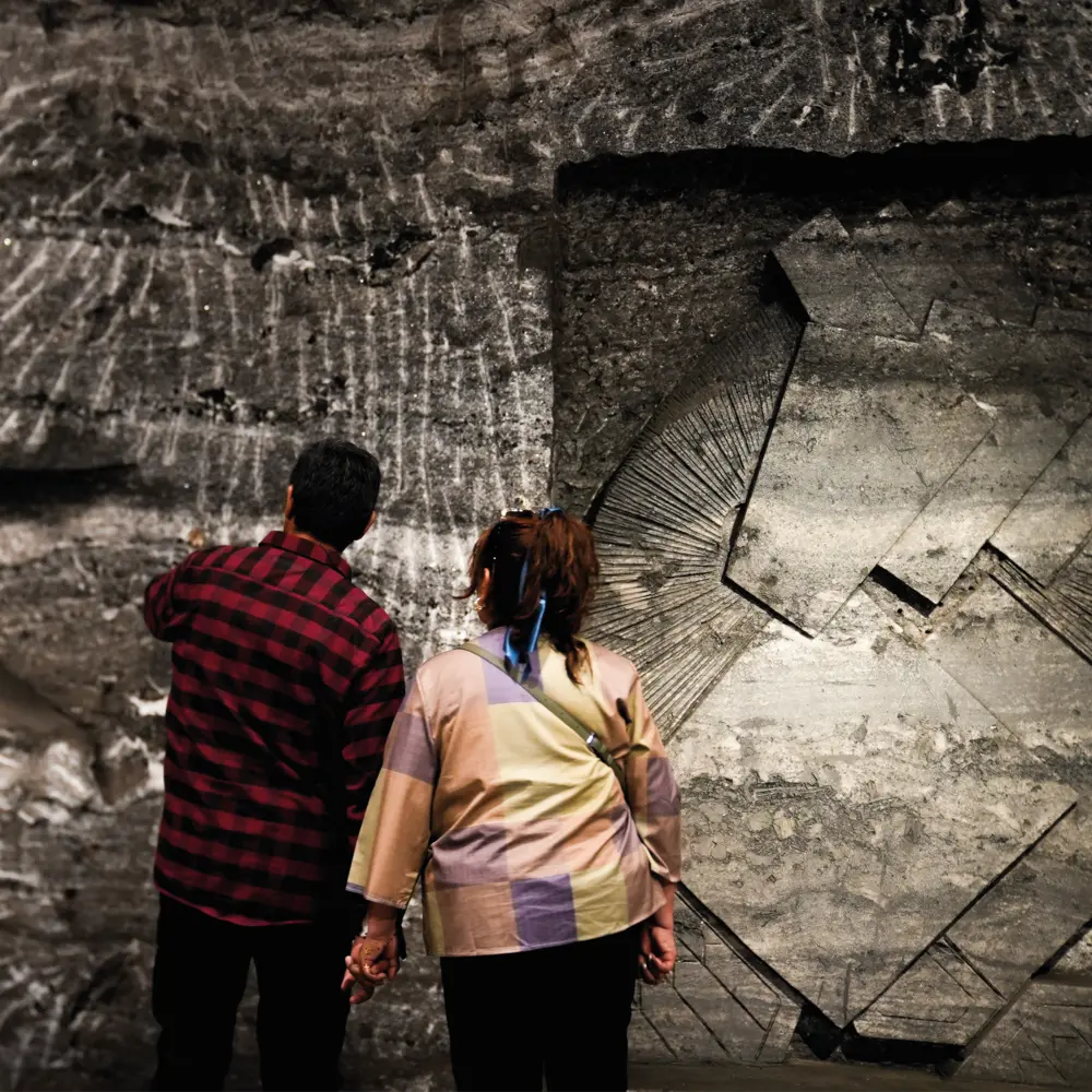 Una pareja camina de la mano y observa una de las estaciones del Viacrucis talladas en relieve sobre los muros de roca de la Catedral de Sal de Zipaquirá.