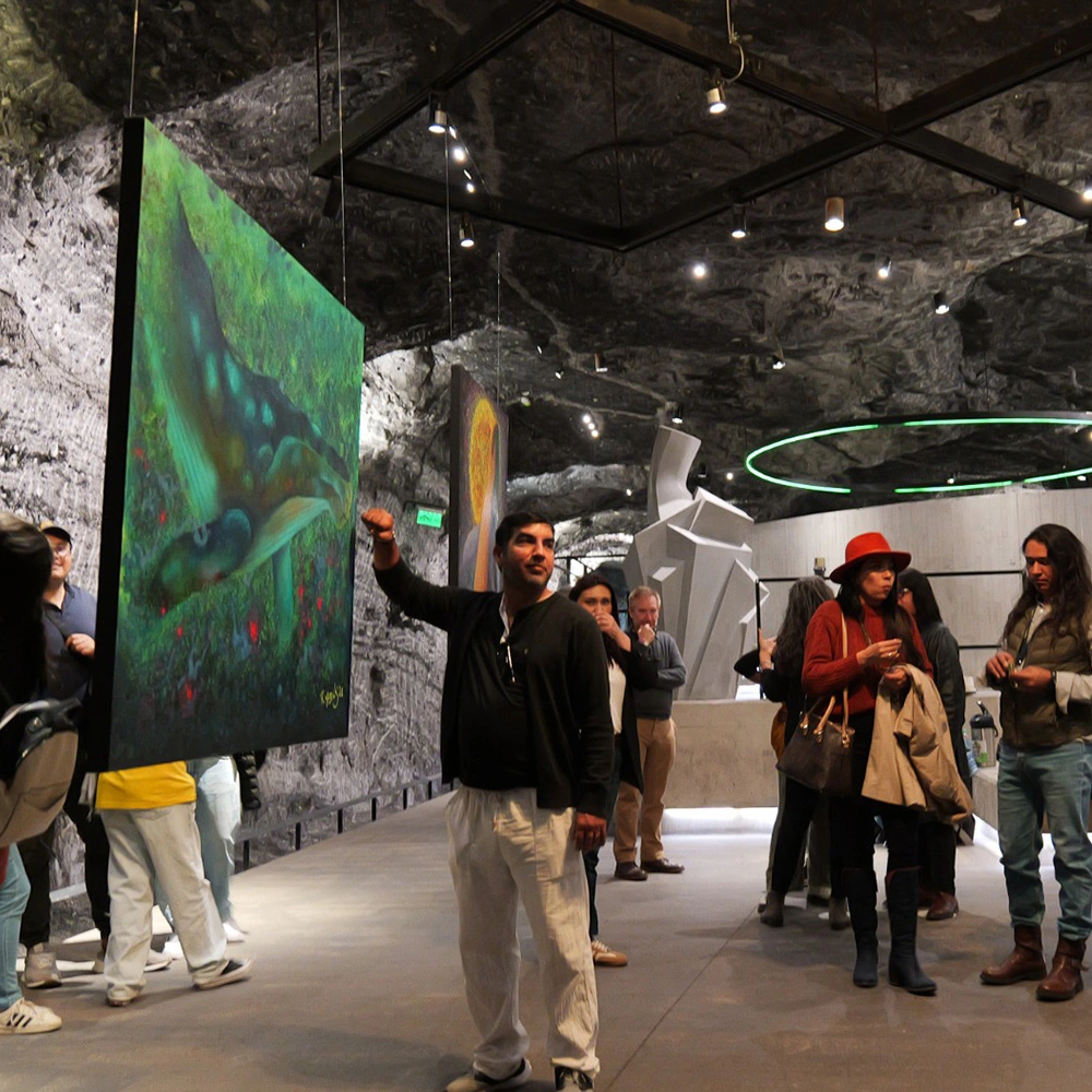 Un grupo de visitantes, liderado por un hombre que señala un cuadro verde flotante con una ballena pintada, recorre la exposición artística subterránea en los túneles tallados en sal de la Catedral de Sal de Zipaquirá