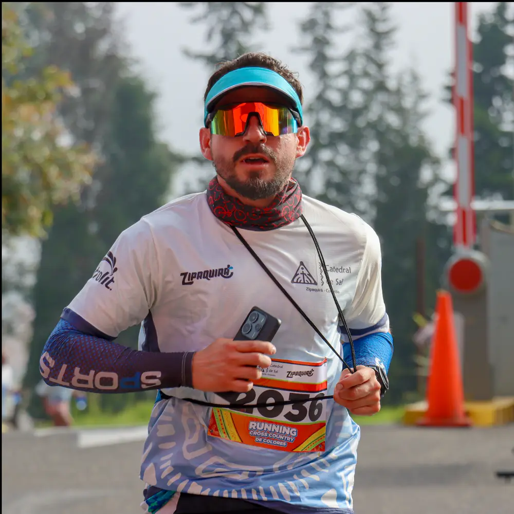 Fotografía de un corredor masculino equipado con visera azul, gafas de sol reflectantes y camiseta oficial corriendo durante la competencia Trail Running de Colores en el Parque de la Sal, Zipaquirá