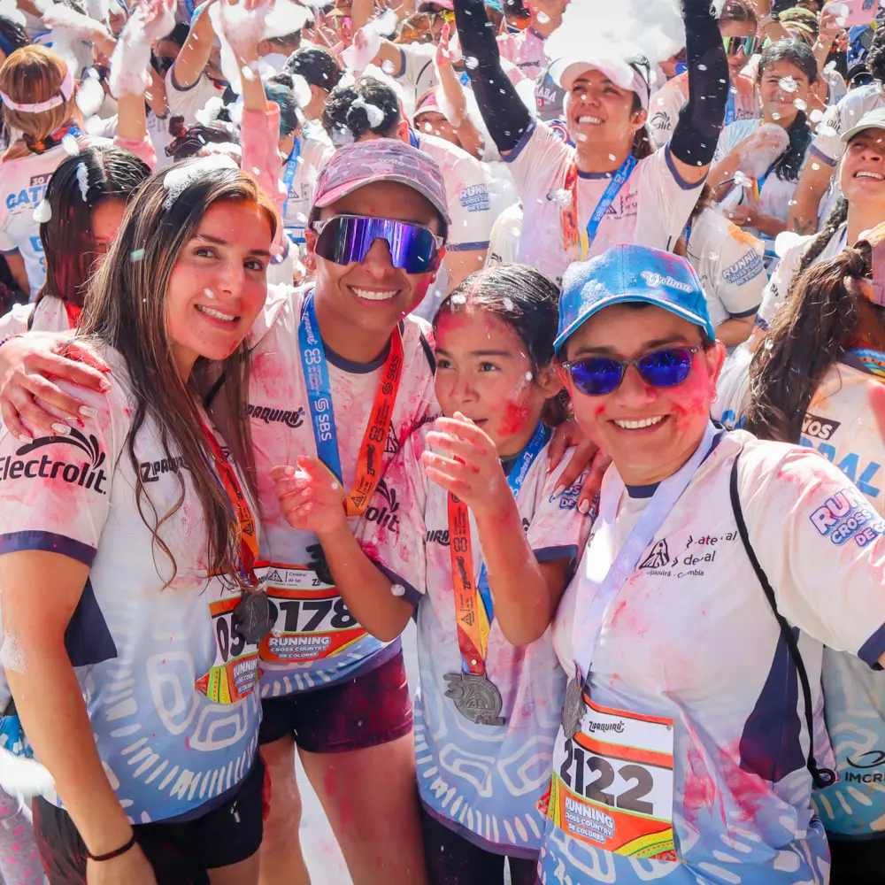 Familia de participantes sonrientes con rostros pintados de colores y camisetas con medallas celebrando entre espuma durante el Trail Running de Colores 2026 en la Catedral de Sal