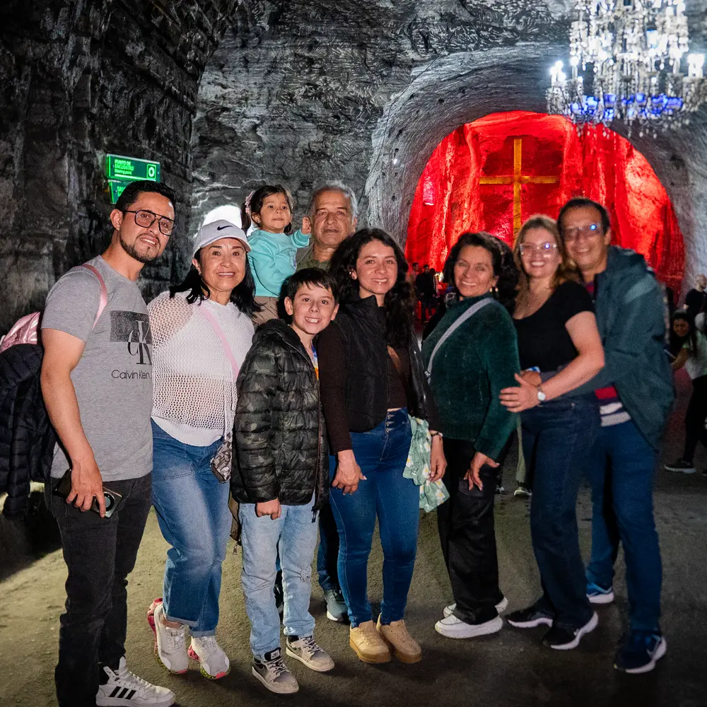 Gran grupo familiar sonriendo juntos en el túnel subterráneo frente a la cruz ilumidada de rojo y la lámpara de araña de cristal en la Catedral de Sal de Zipaquirá