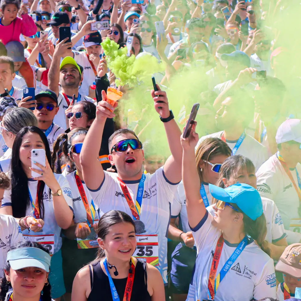 Grupo de corredores y asistentes alegres celebrando con humo y polvo de color verde durante el evento Trail Running de Colores 2026 en Zipaquirá